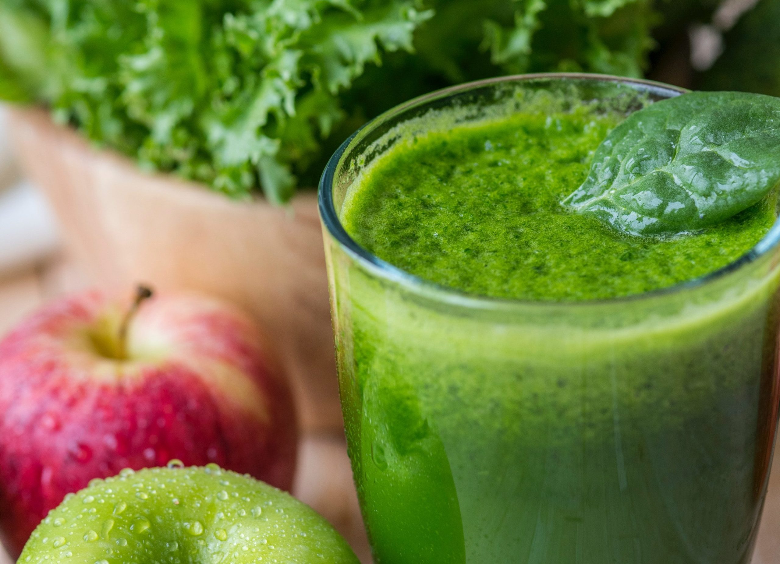 Green smoothie in glass surrounded by fruit.